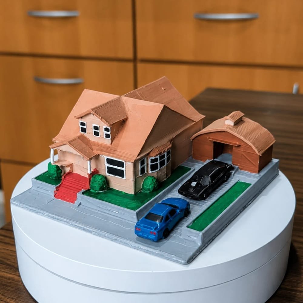 Maquete de uma casa com varanda, garagem e gramado, com dois carros em miniatura na entrada